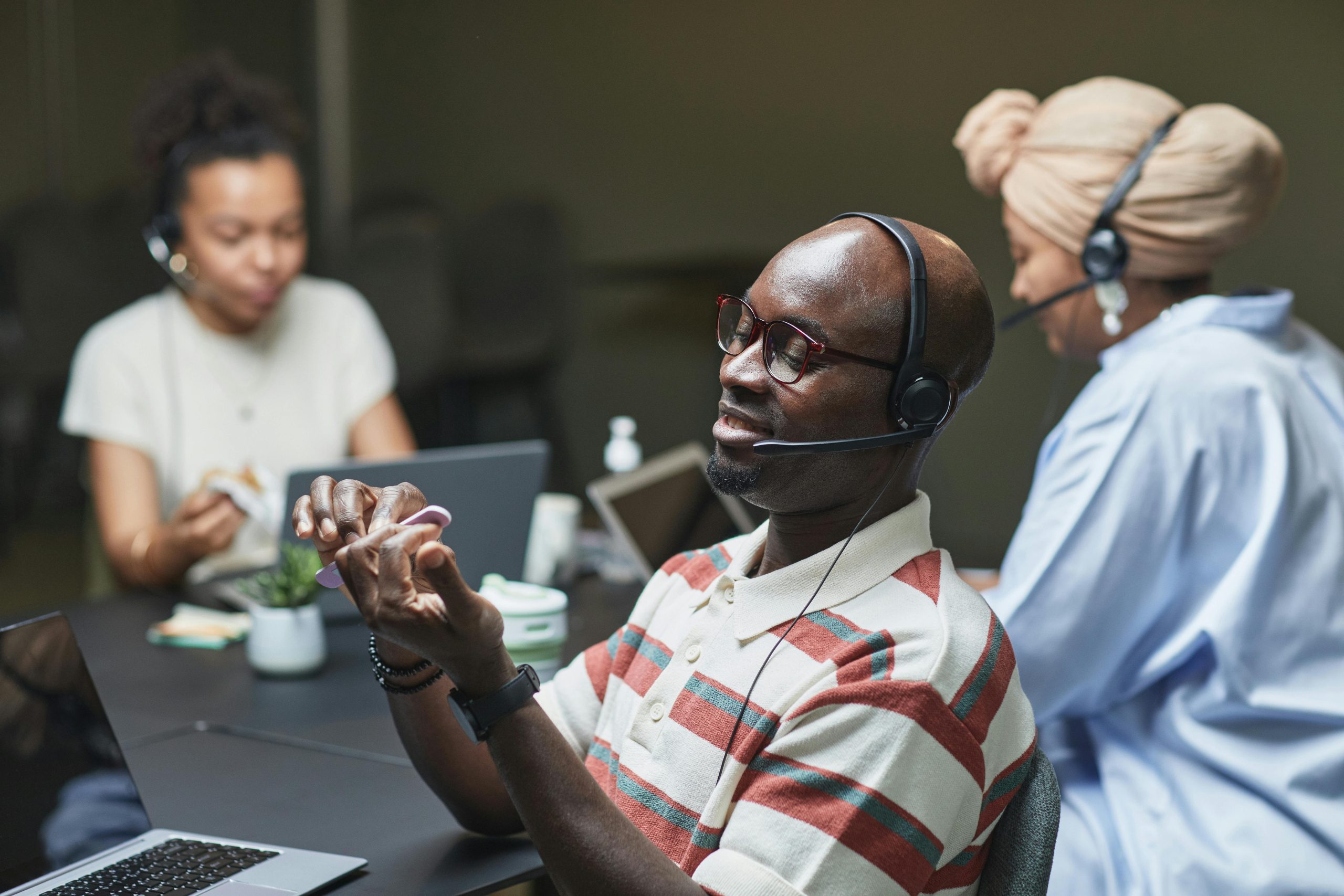 A group of diverse professionals working at a call center desk, engaged with laptops and headsets.